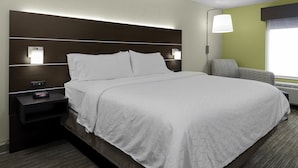 A hotel room with a large bed, a nightstand with a lamp, and a chair by the window. - Holiday Inn Express Hotel & Suites CORDELE NORTH by IHG (Cordele)