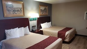 Habitación de hotel con dos camas, una mesita de noche con lámpara y dos cuadros enmarcados en la pared.