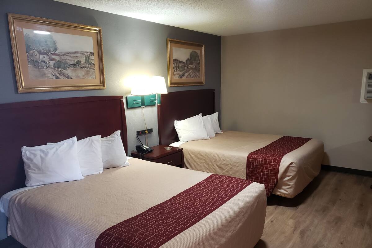 A hotel room with two beds, a nightstand with a lamp, and two framed pictures on the wall.