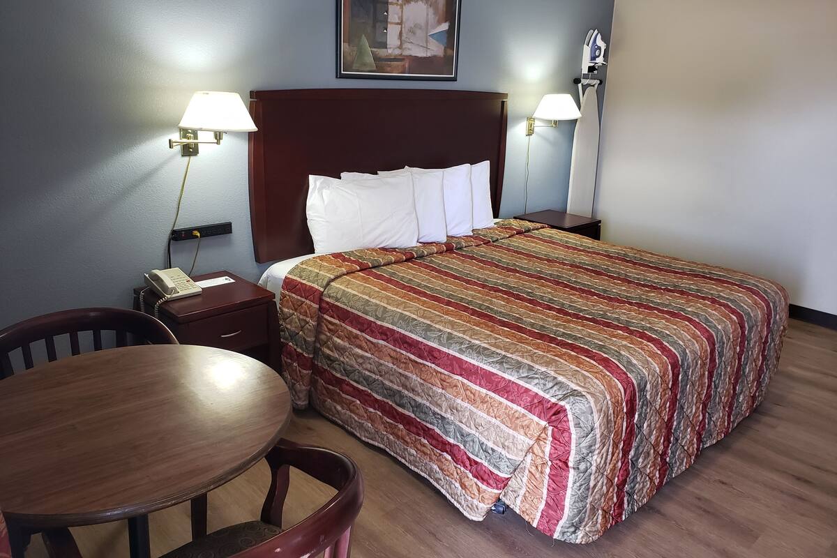 A hotel room with a bed, two bedside lamps, a telephone, a wooden table, and a chair.