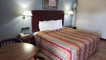 A hotel room with a bed, two bedside lamps, a telephone, a wooden table, and a chair.