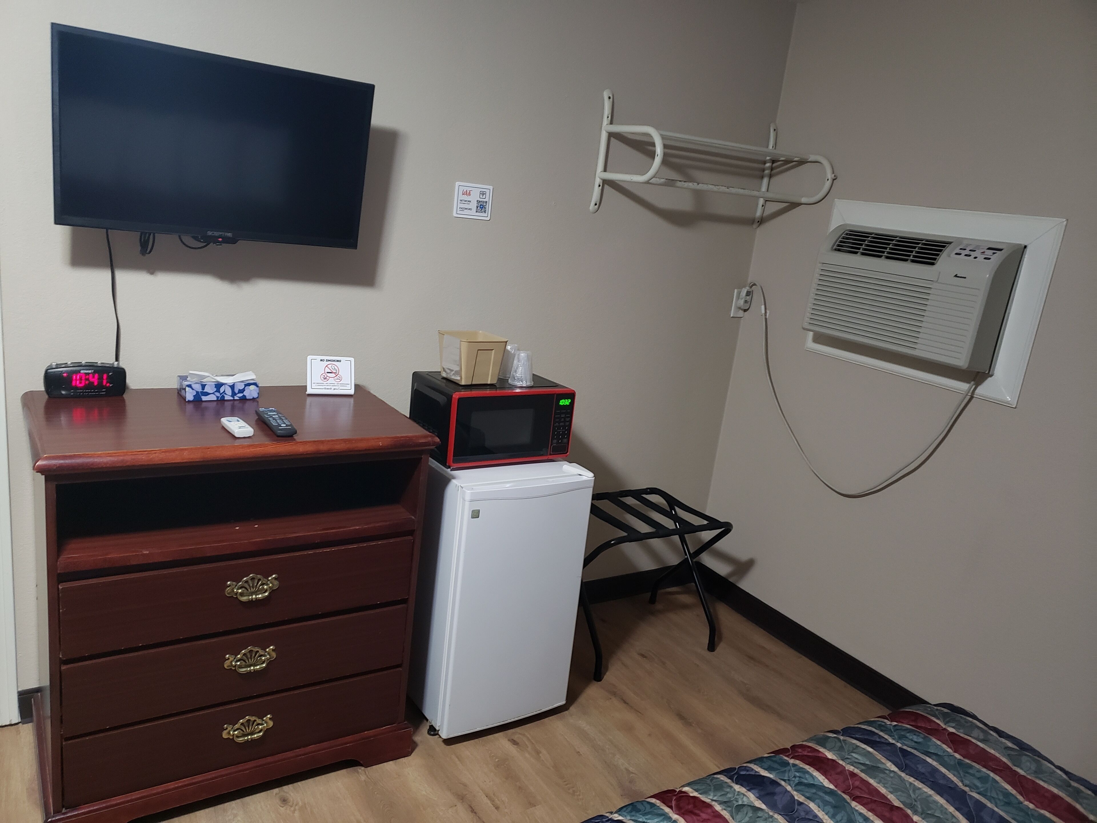 A small room with a wooden dresser, a microwave, a television, and a small refrigerator.