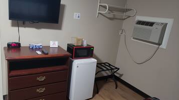 A small room with a wooden dresser, a microwave, a television, and a small refrigerator.