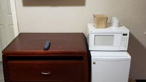 Una kitchenette compacta con microondas, un refrigerador pequeño y un televisor montado en la pared.