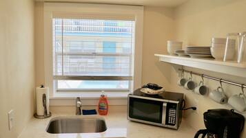 A compact kitchen with a sink, a microwave, a coffee maker, and a window with blinds.