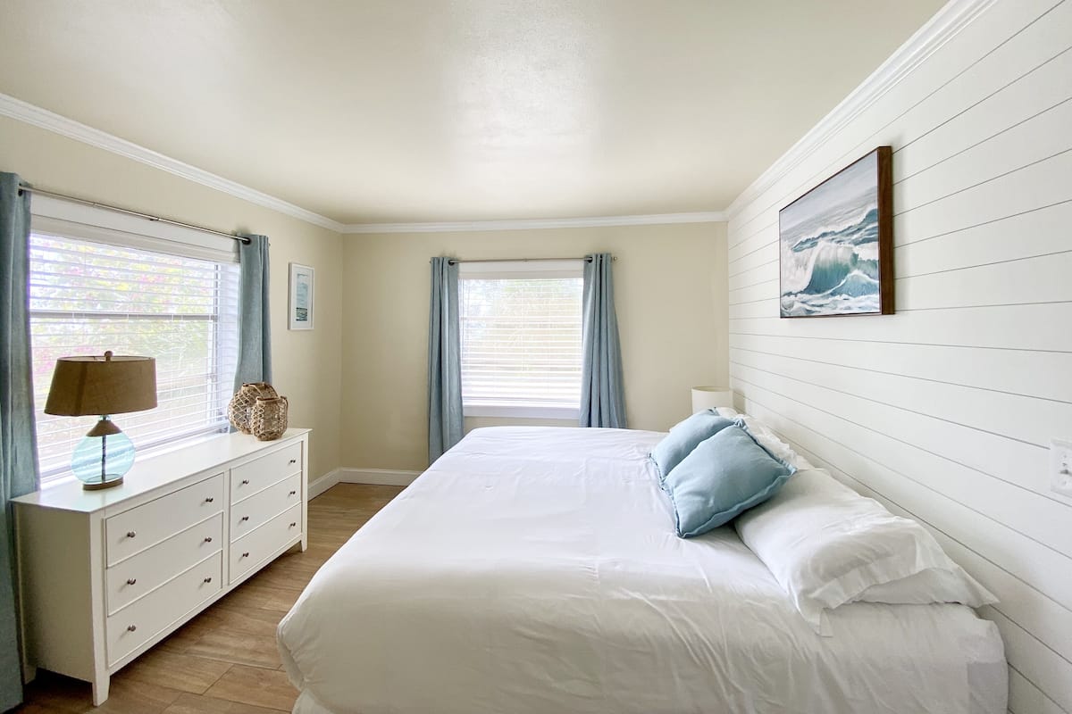 Une chambre à coucher avec un lit, une commode, une lampe et un tableau au mur.
