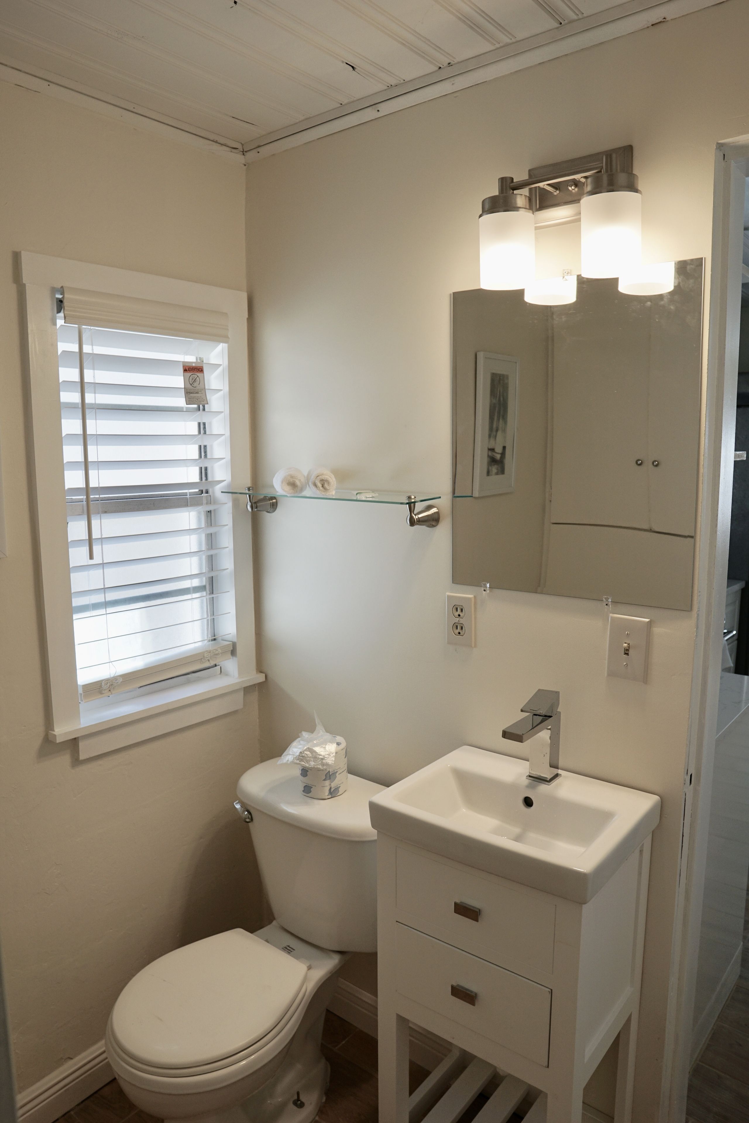 Een badkamer met toilet, wastafel, spiegel en raam met zonwering.