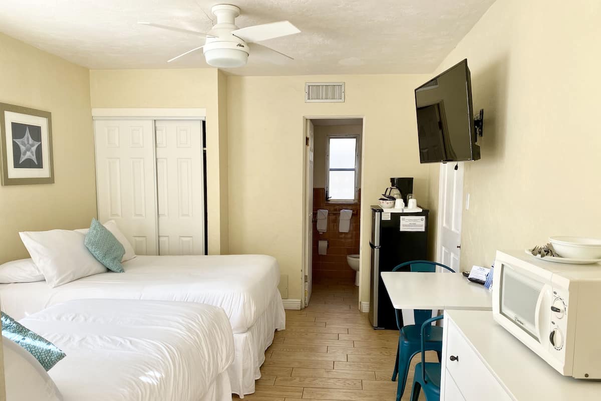 Une chambre d’hôtel avec un lit, un bureau doté d’un micro-ondes, une télévision et une salle de bain visible au fond.