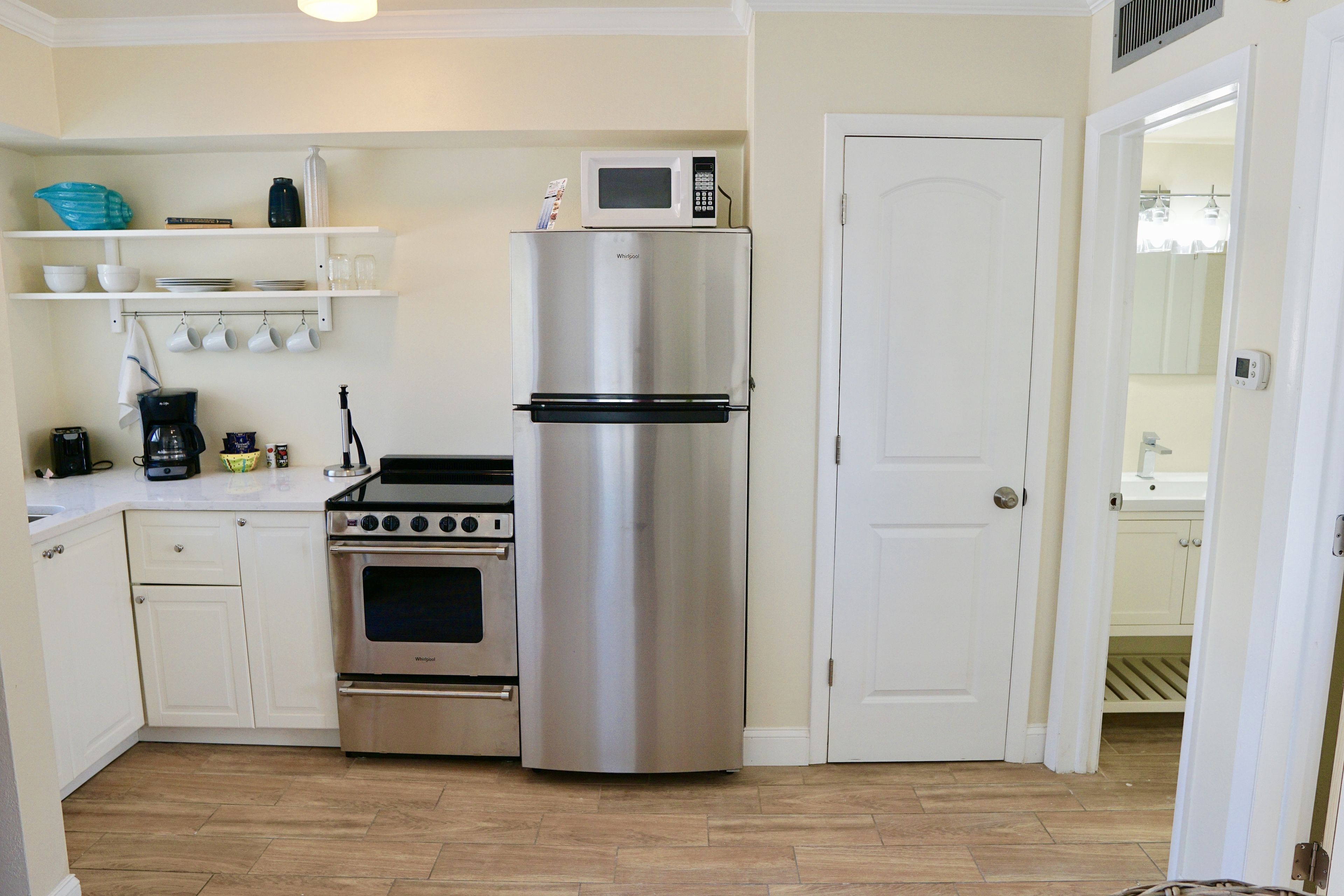 A compact kitchen with a stainless steel refrigerator, a built-in oven, and a microwave on top.