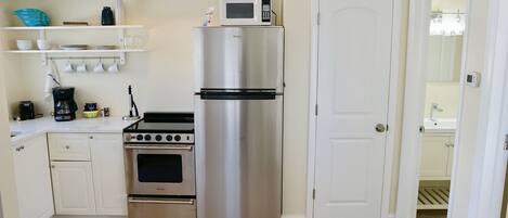 A compact kitchen with a stainless steel refrigerator, a built-in oven, and a microwave on top.