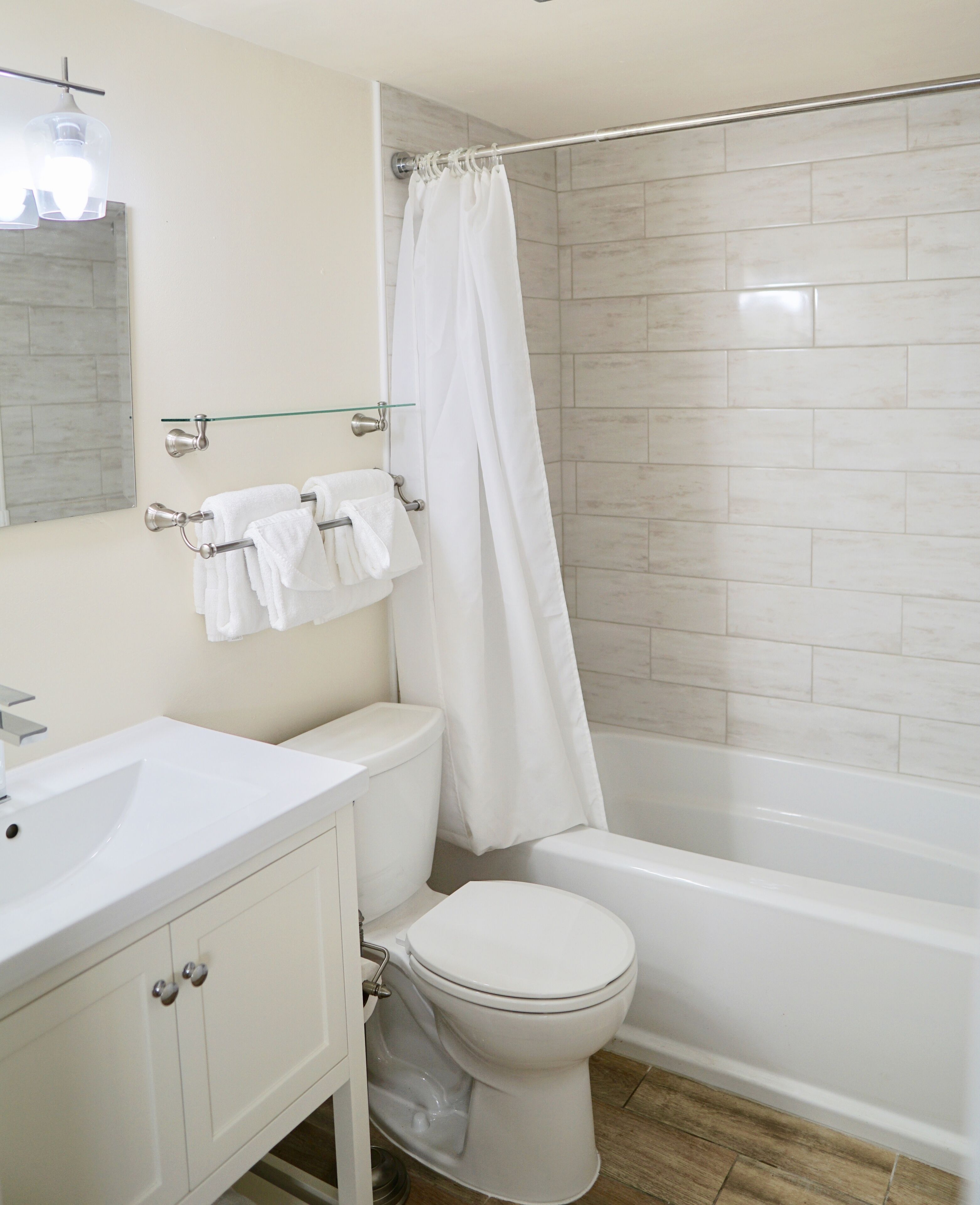 A bathroom with a white sink, toilet, and bathtub. There is a glass shelf above the sink holding a towel.