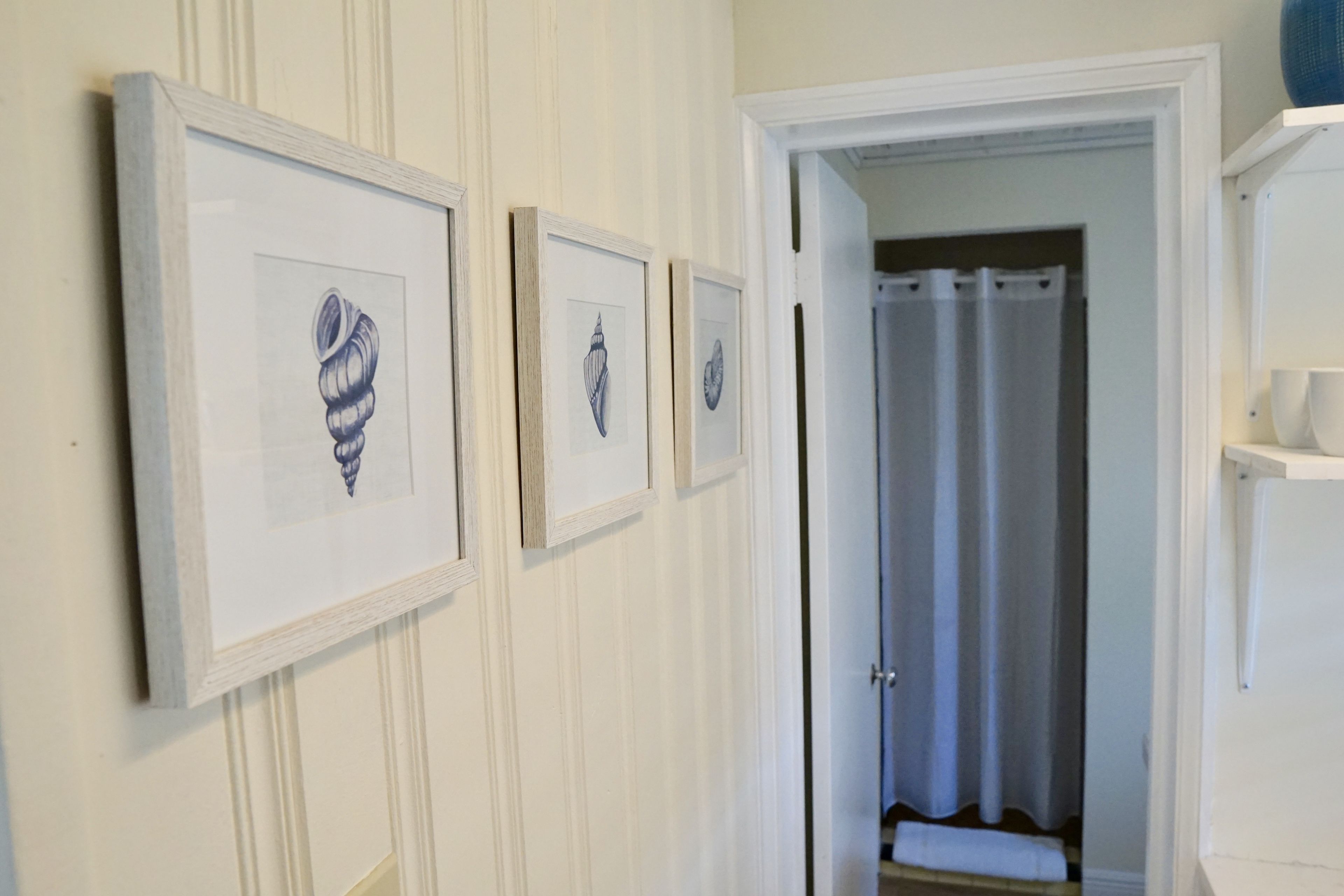 Ein Flur mit gerahmten Kunstwerken an der Wand und einer Tür zu einem Badezimmer.