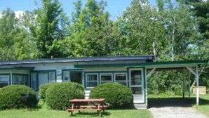 A two-story building with a green roof, a covered outdoor seating area, and a gravel driveway. - Patio Motor Court (Twin Mountain)
