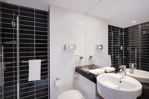 A modern bathroom with black and white tiles, a glass shower enclosure, and two sinks. - Holiday Inn Express Bremen Airport by IHG (Bremen)