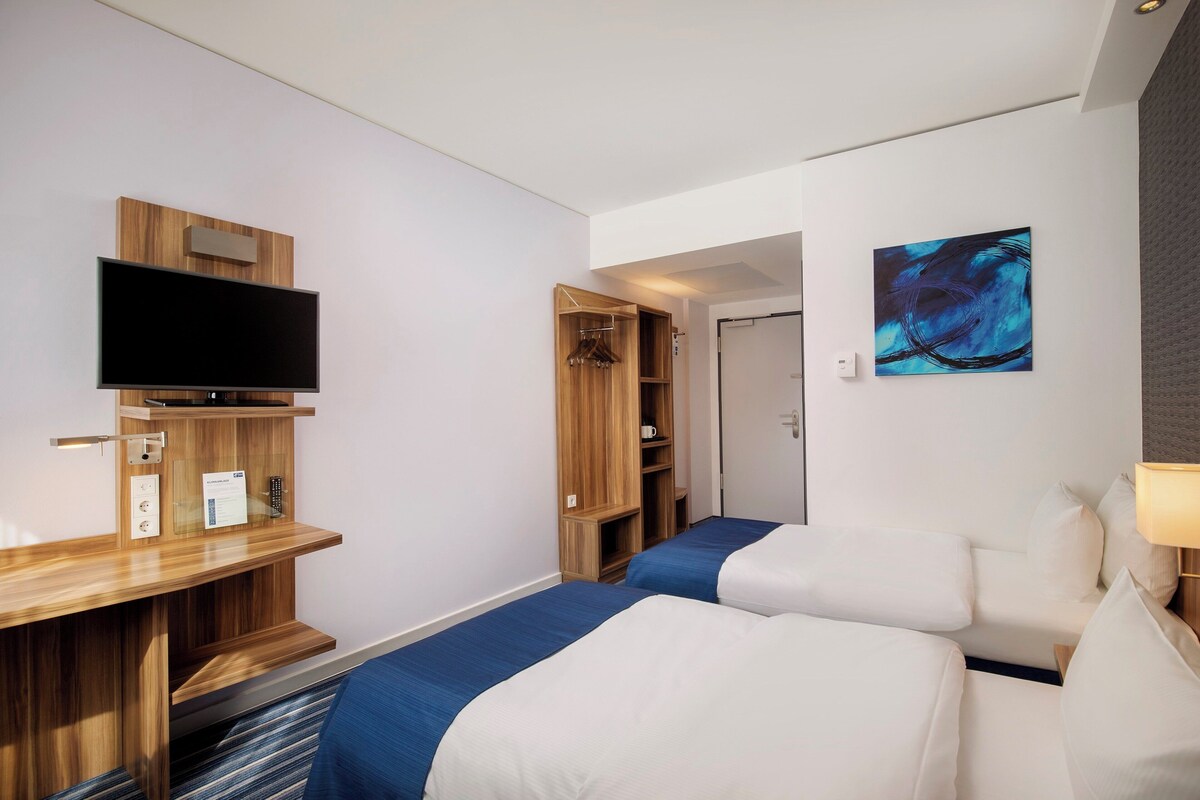 A hotel room with a TV, a desk, two beds, a wardrobe, and a painting on the wall.