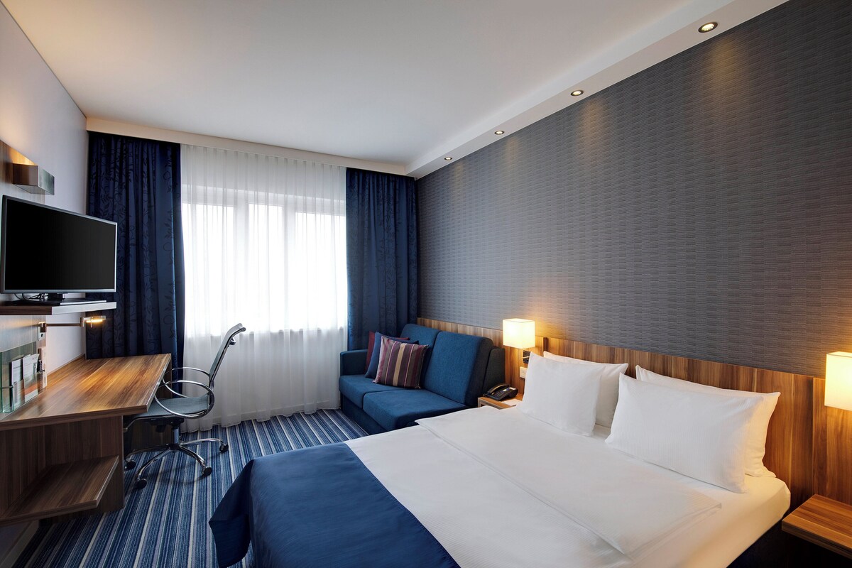 A hotel room with a bed, a desk, a television, and a sofa.