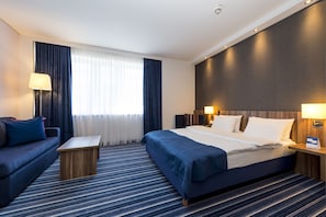 A hotel room with a bed, a sofa, a small table, and a nightstand with lamps. - Holiday Inn Express Bremen Airport by IHG (Bremen)