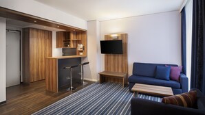 A modern hotel room with a kitchenette, a flat-screen TV, a sofa, and a striped rug. - Holiday Inn Express Bremen Airport by IHG (Bremen)