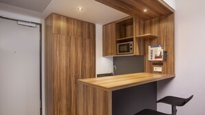 A compact kitchen with wooden cabinetry, a microwave, and a small bar area with two stools. - Holiday Inn Express Bremen Airport by IHG (Bremen)