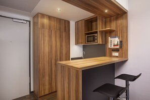 A compact kitchen with wooden cabinetry, a microwave, and a small bar area with two stools. - Holiday Inn Express Bremen Airport by IHG (Bremen)