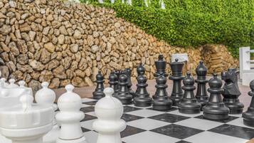 A chessboard with pieces set up, surrounded by a stone wall and greenery.