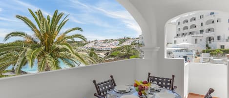 A round table with chairs and a view of a beach and buildings in the background.