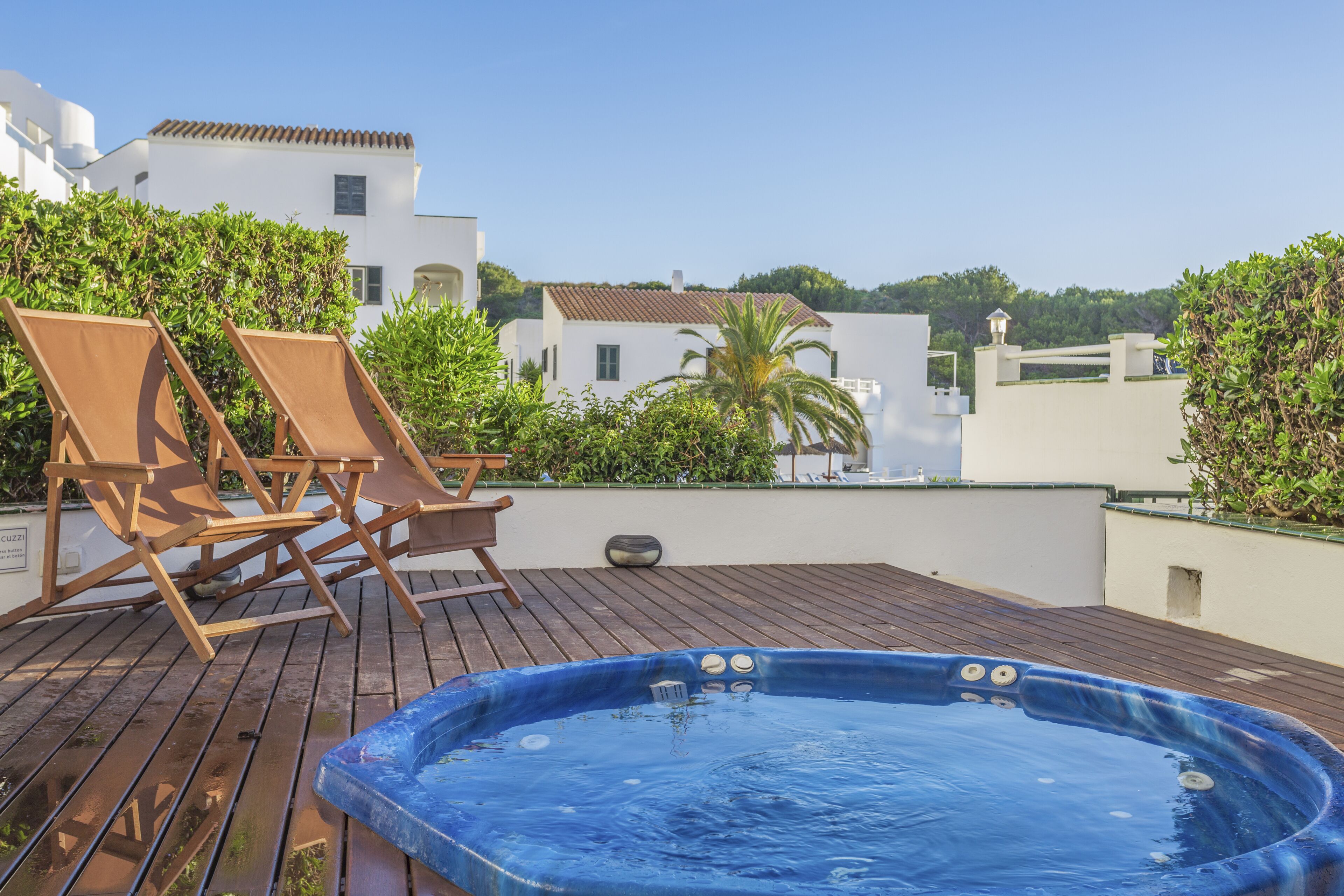 A rooftop deck with a hot tub, lounge chairs, and a view of surrounding buildings.