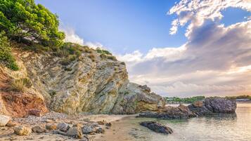 A coastal landscape with a rocky cliff, beach, and calm sea.