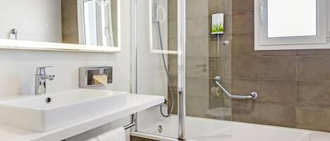 Un bany modern amb un lavabo blanc, un mirall i una dutxa amb envàs de vidre.