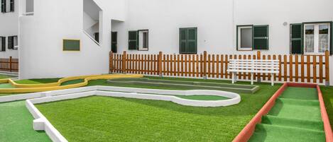 A courtyard with artificial grass, a wooden fence, and a white bench.