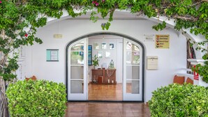 An entrance with a glass door, a reception desk, and a sign indicating currency exchange services. - White Sands Beach Club (Mercadal)