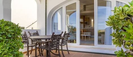 Un patio con mesa y sillas, una puerta de cristal que da a una cocina y vistas al cielo.