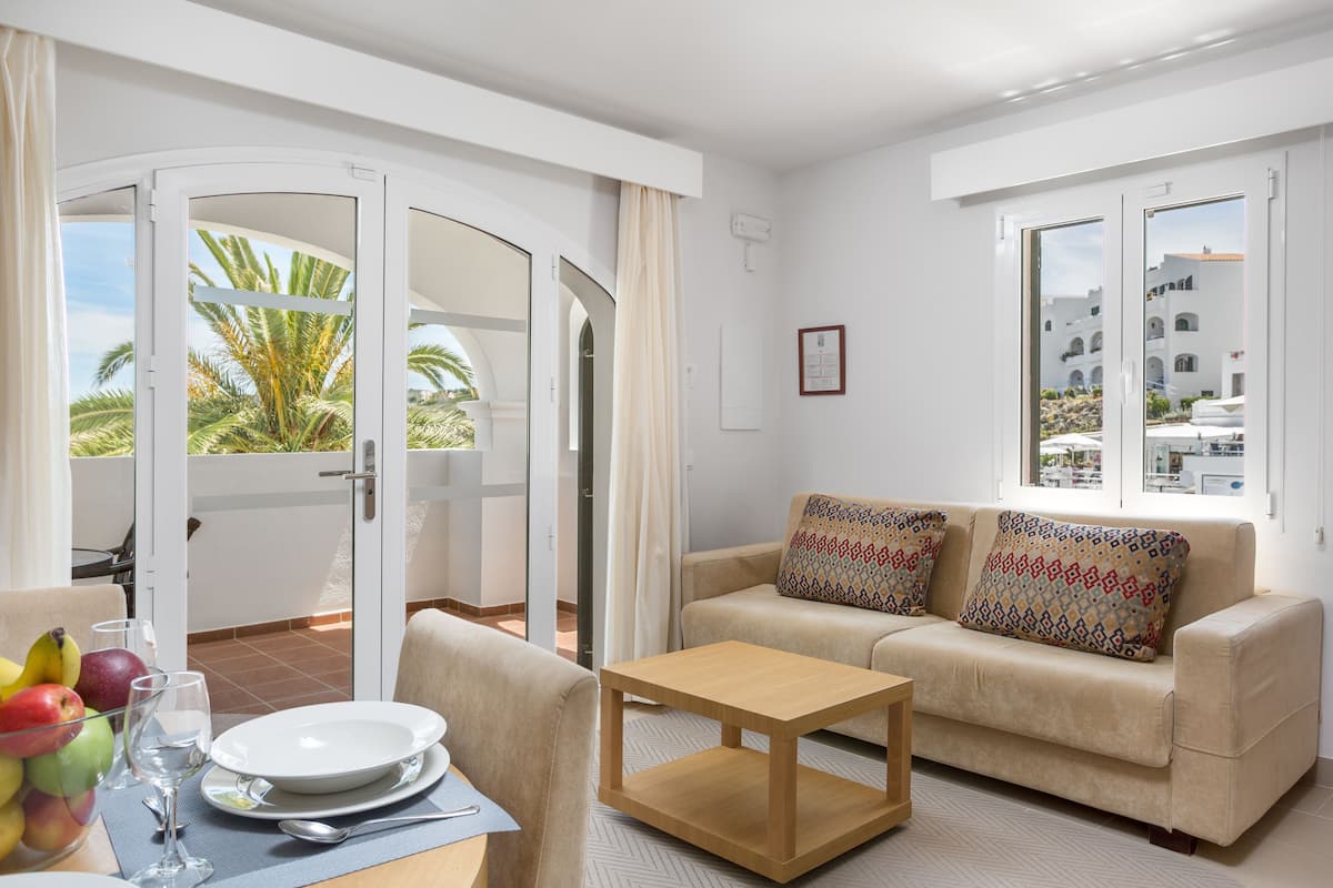 A modern living room with a sofa, a wooden coffee table, and a dining table set for two.