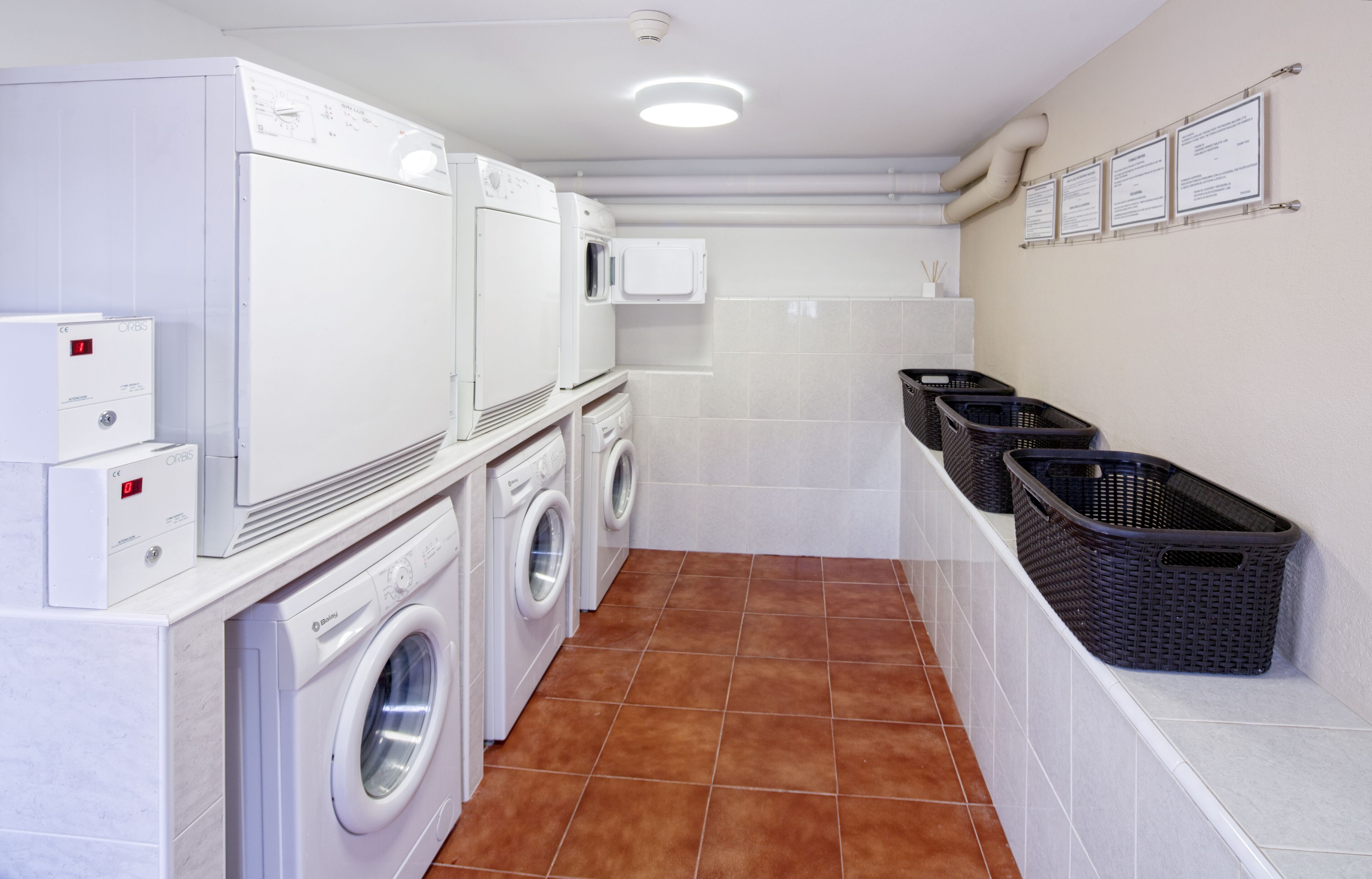A laundry room with a front-loading washer and dryer, a microwave, and baskets for laundry.