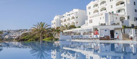 Un complexe hôtelier doté d’une piscine, de bâtiments blancs et d’un palmier.