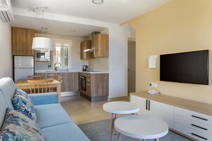 Una sala de estar moderna con un sofá, una mesa de comedor y una zona de cocina con armarios de madera y un televisor de pantalla plana.