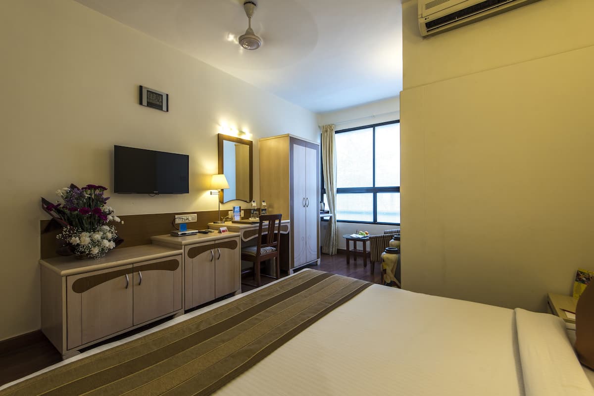 Habitación de hotel con cama, escritorio, silla, televisor, espejo y ventana.