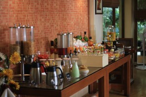 Montaje tipo buffet con diferentes alimentos y bebidas, una estación de café y un jarrón decorativo con flores.