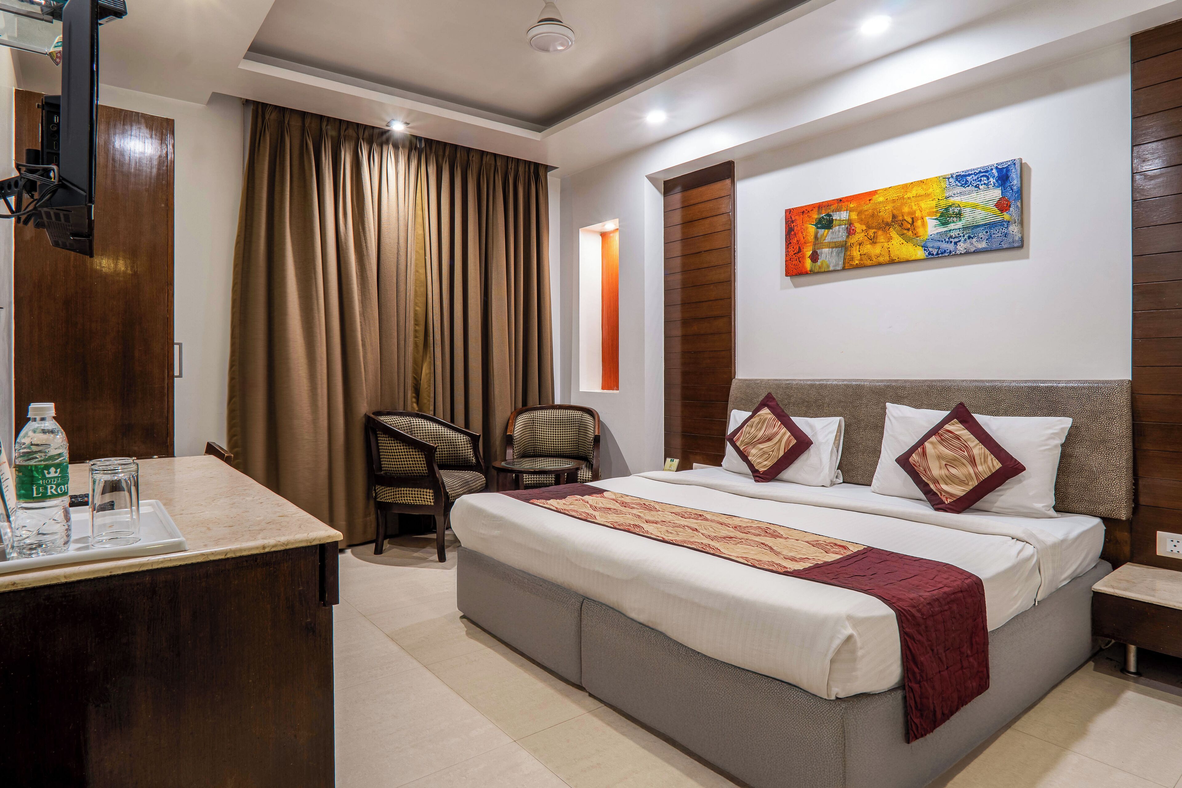 A hotel room with a large bed, a desk with a chair, a TV, and a painting on the wall.