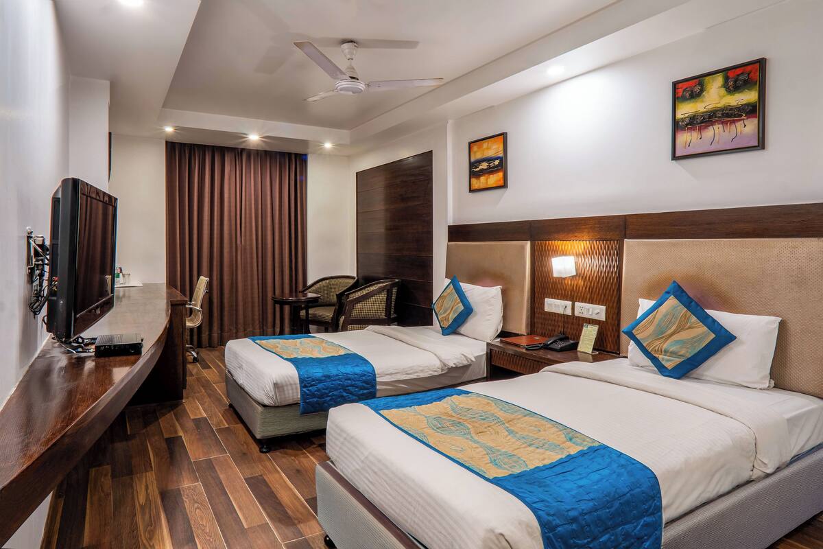 A hotel room with two beds, a desk, a TV, and a ceiling fan.