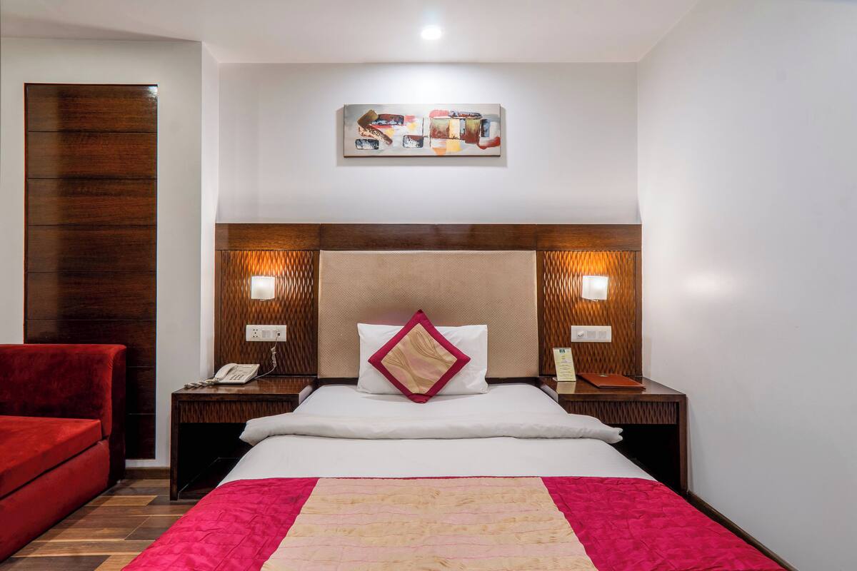 A hotel room with a large bed, two bedside tables with lamps, a red chair, and a wooden headboard.