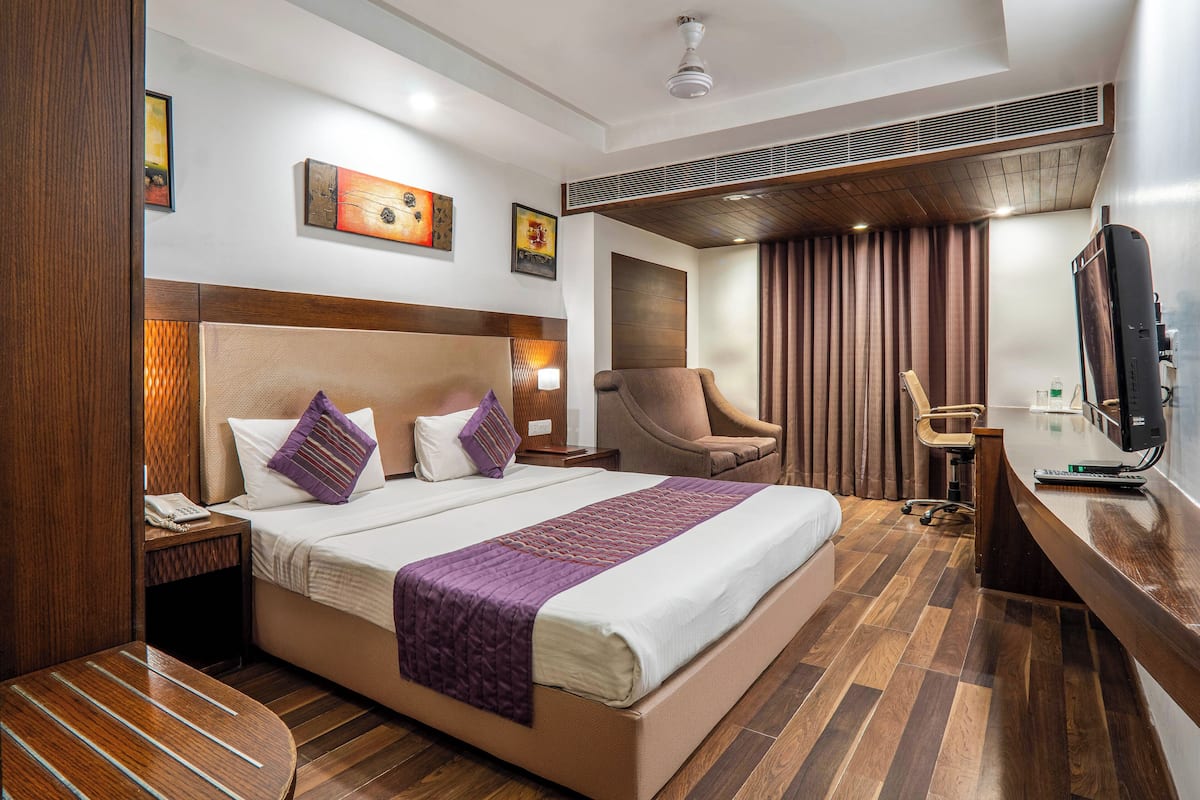 A hotel room with a large bed, a desk, a chair, and a television.