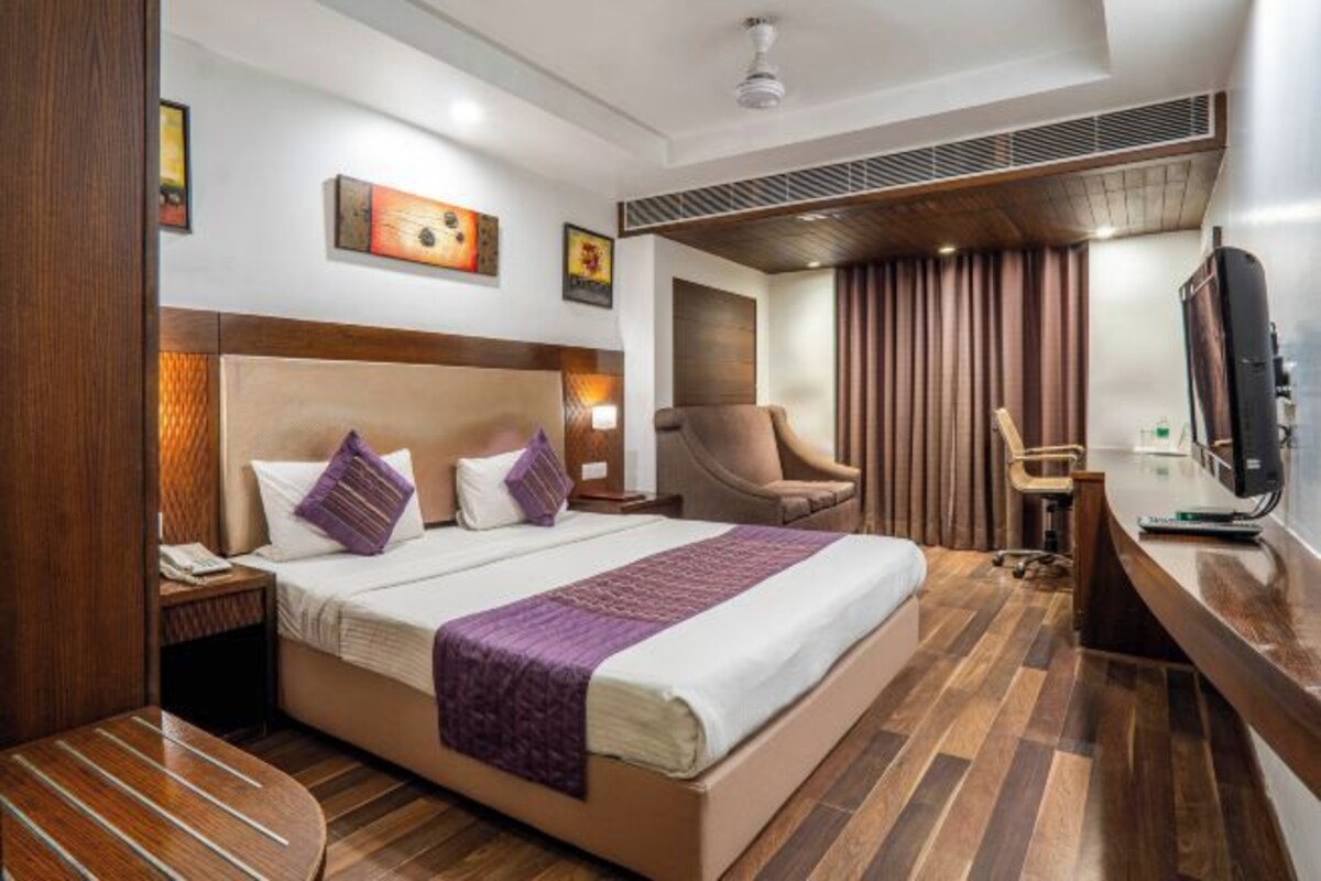 A hotel room with a large bed, a desk, a chair, and a television.
