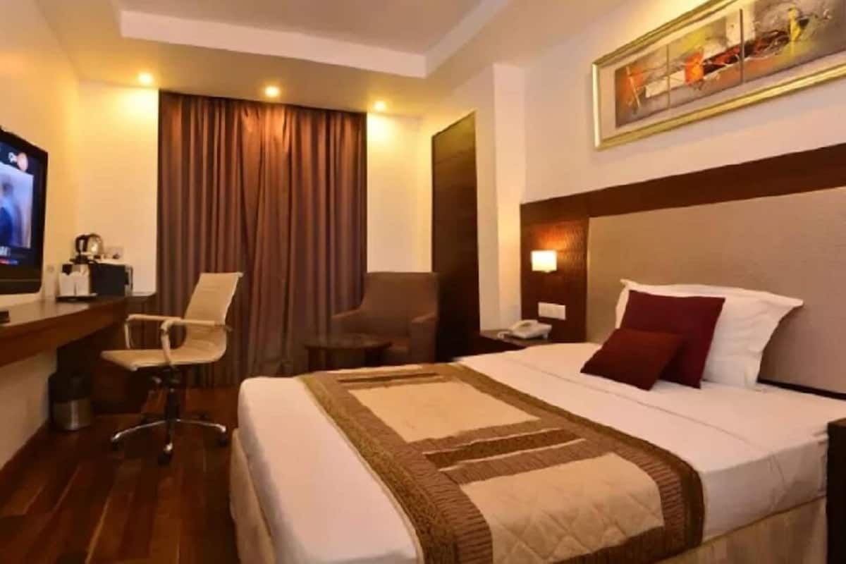 A hotel room with a bed, a desk with a chair, a television, and a painting on the wall.