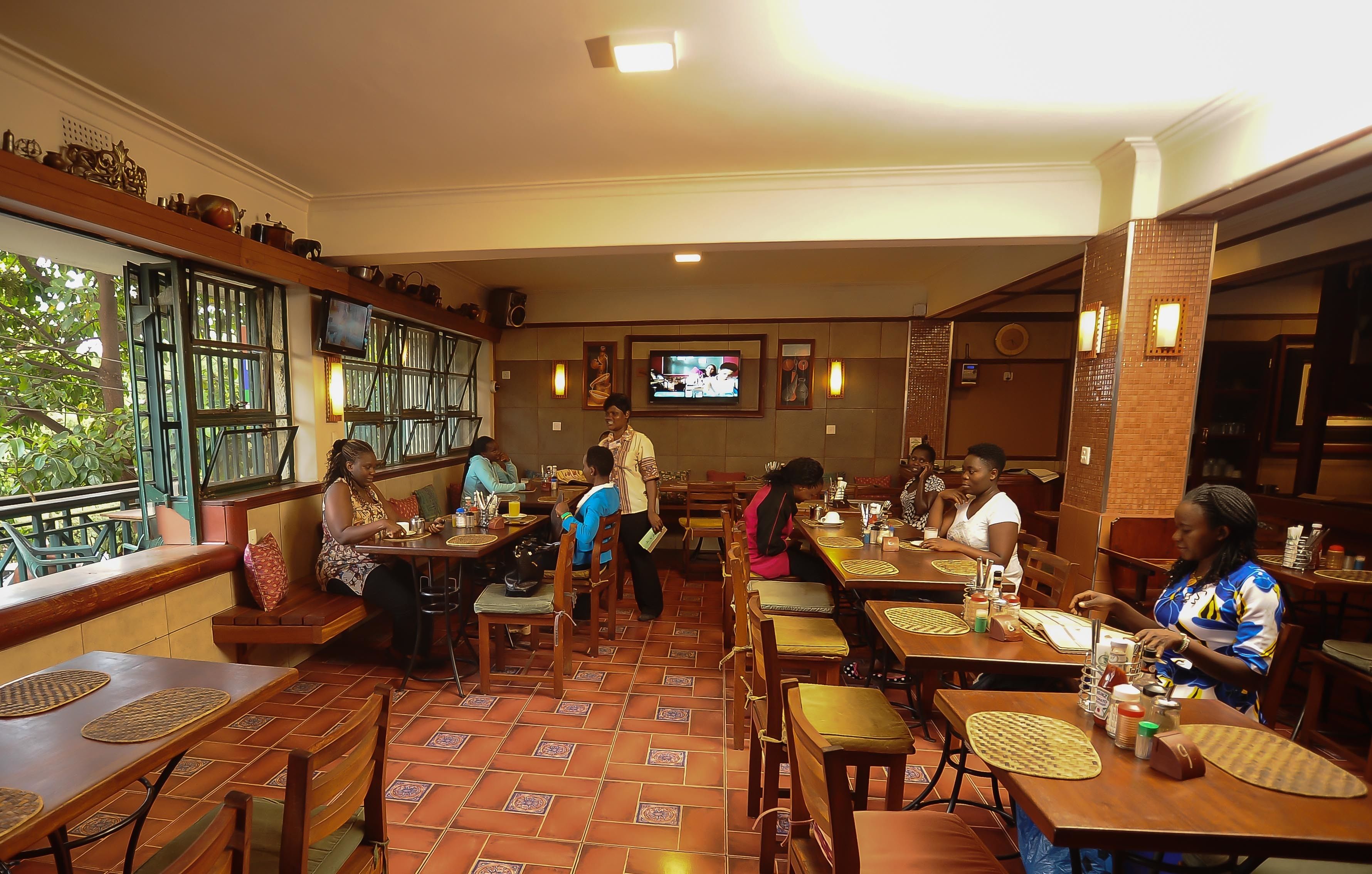 A restaurant with wooden tables and chairs, a television mounted on the wall, and a tiled floor.