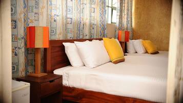 Habitación de hotel con dos camas, cabeceros de madera, ropa de cama blanca y cortinas estampadas.