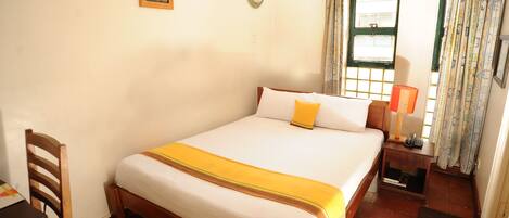 A neatly arranged bedroom with a bed, a chair, a bedside table with a lamp, and a window with curtains.