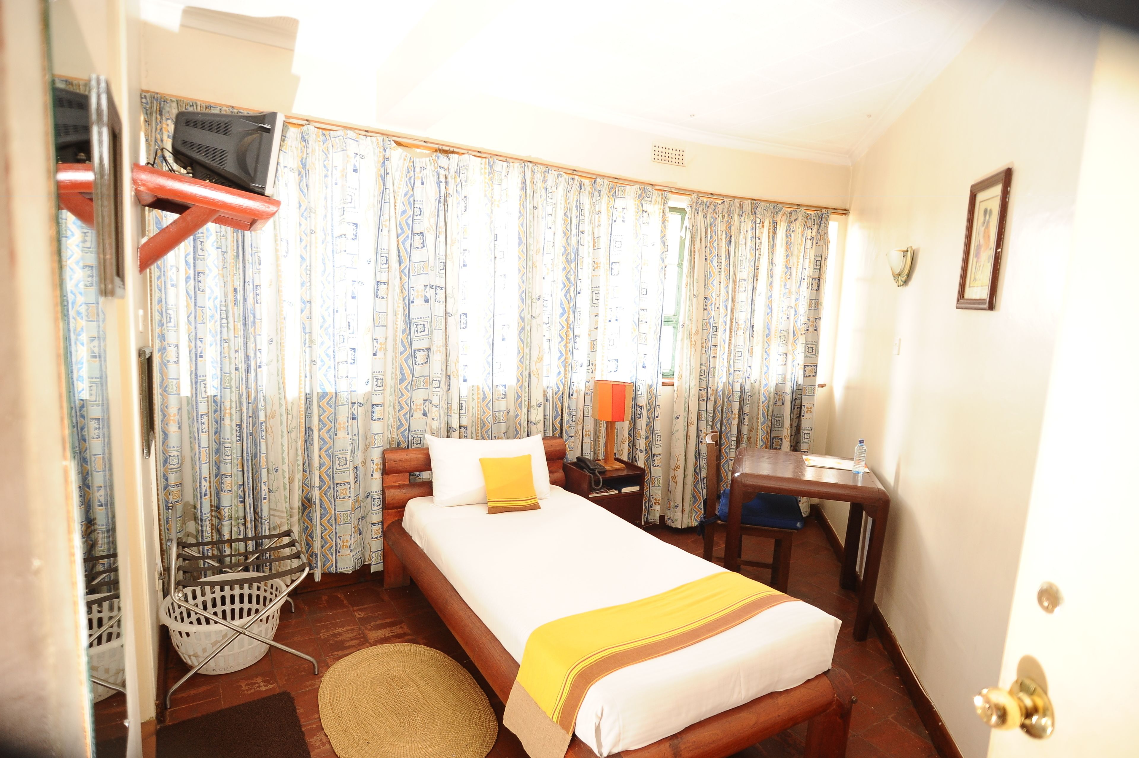 A hotel room with a bed, a desk, a chair, a television, a lamp, and curtains.