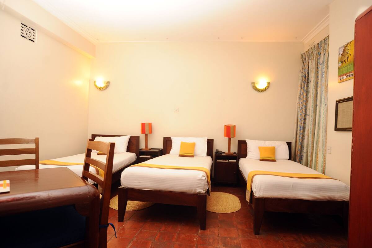 Ein Hotelzimmer mit zwei Einzelbetten, einem Holzstuhl, einem kleinen Tisch und zwei Nachttischlampen.