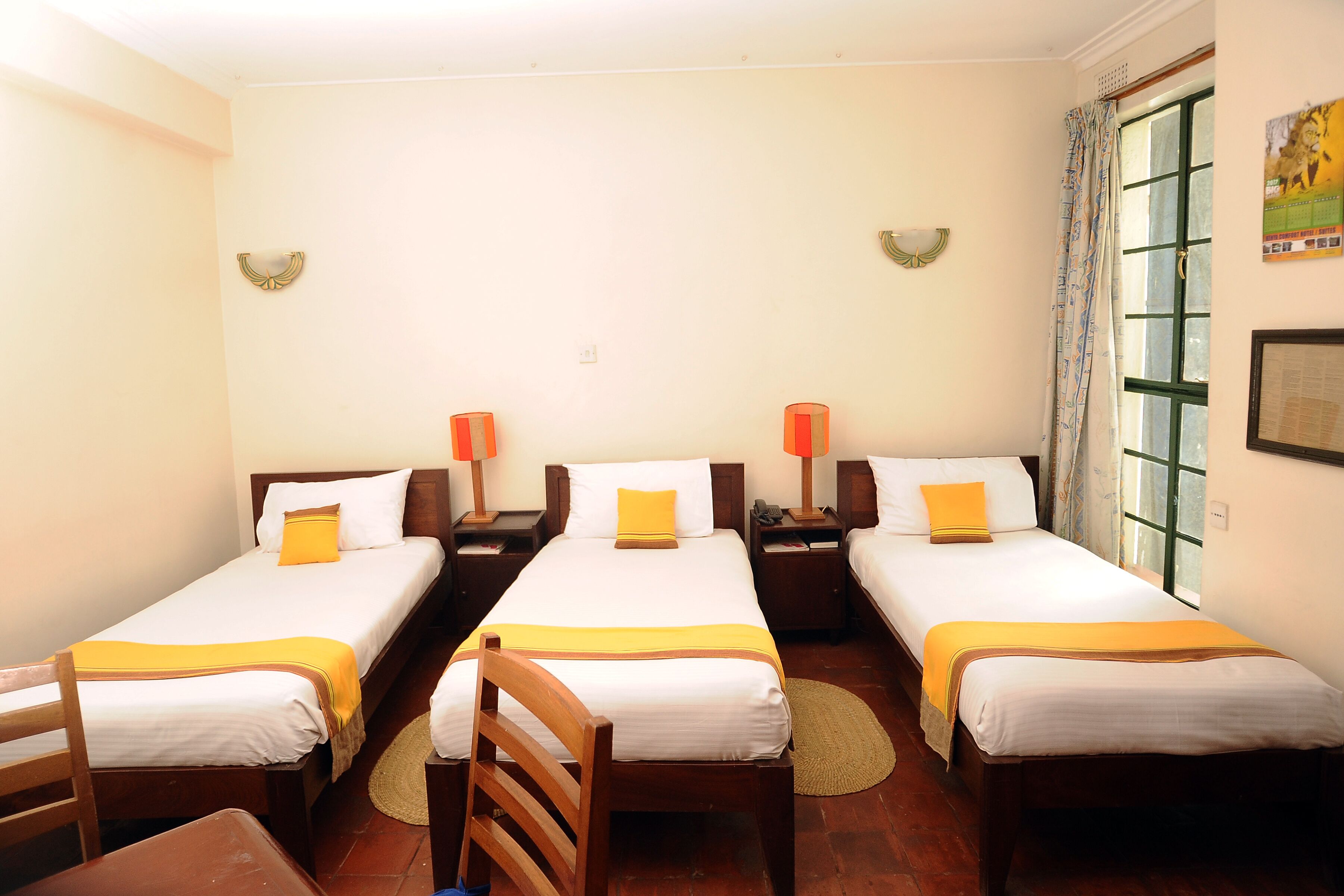 Habitación de hotel con tres camas individuales, cada una con un cojín amarillo decorativo, cabeceros de madera y lámparas de noche.